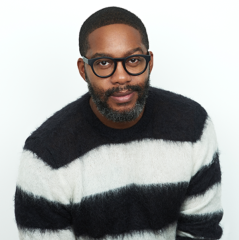 A man with dark skin, short hair and glasses wearing a black and white sweater.