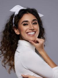 Woman with medium-tone skin and dark curly hair wearing a white hair bow and turtleneck sweater.