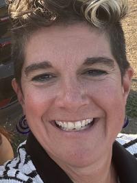 A woman with short-cropped curly hair wearing a white polo with black stripes. 
