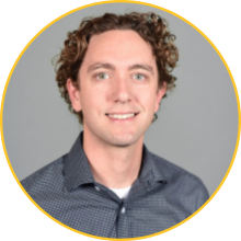 Man with fair skin and curly brown hair wearing a gray button up shirt