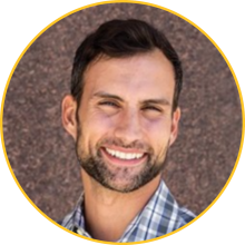 Man with fair skin, dark hair and a salt and pepper beard wearing a plaid button up shirt